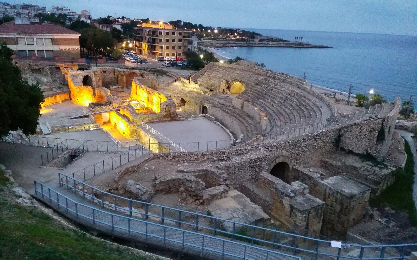 Tarragona's illuminated Roman amphitheatre between the city and the Mediterranean